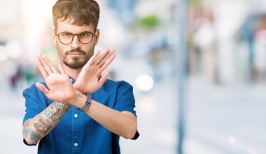 Yakışıklı delikanlı izole arka plan ret ifade geçiş silah ve avuç içi eksi işareti, kızgın surat yapıyor üzerinde gözlük