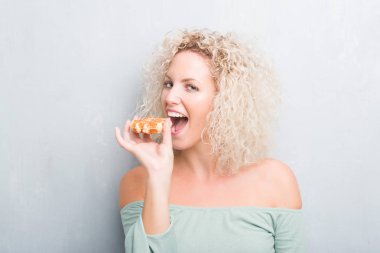 Sarışın genç kadın kendine güvenen bir ifade ile Belçika waffle ciddi düşünme akıllı yüzünde yeme grunge gri arka plan üzerinde