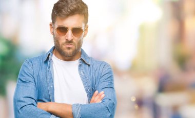 Genç yakışıklı adam izole arka plan şüpheci ve sinir, onaylamayan ifade yüz çapraz kolları üzerinde güneş gözlüğü takıyor. Negatif kişi.