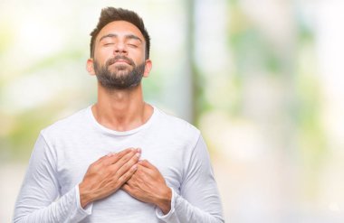 Göğüs kapalı gözler ve yüzünde minnettar jest ile yetişkin İspanyol adam ile gülümseyen izole arka plan üzerinde eller. Sağlık kavramı.