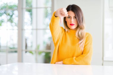 Evde kış kazak giyen genç güzel kadın mutsuz ve kızgın ret gösterilen ve başparmak aşağı hareketi ile negatif arıyorum. Kötü ifade.