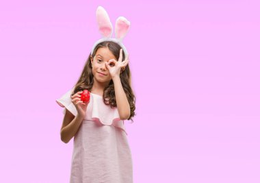 Esmer İspanyol kız mutlu yüz el parmaklarının arasından seyir göz üzerinde ok işaretiyle yapıyor gülümseyen ile Paskalya tavşan kulakları giyiyor