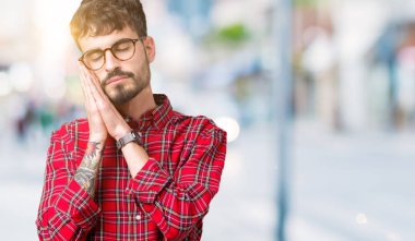 Uyku yorgun hayal ve ellerle birlikte poz ile kapalı gözler gülümseyen izole arka plan üzerinde gözlük takan genç yakışıklı adam.