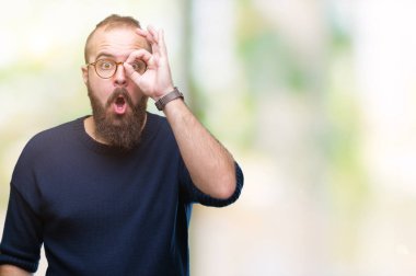 Sürpriz yüz, göz parmaklarının arasından seyir ile ok jest yapıyor izole arka plan üzerinde güneş gözlüğü takmış Genç beyaz hipster adam şok. İmansız ifade.
