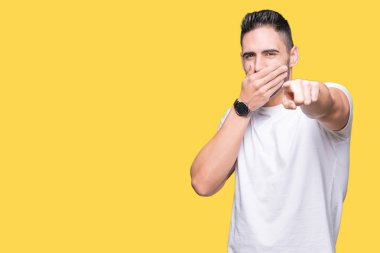 Yakışıklı adam izole sarı üzerinde beyaz t-shirt giyen gülme sizin arka plan, fotoğraf makinesi ile işaret eden parmak el ağzına, utanç ifadesi