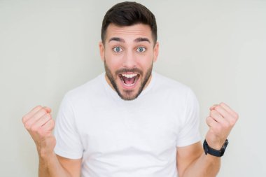 Yakışıklı delikanlı izole arka plan kutlama üzerinde rahat beyaz t-shirt giyen şaşırttı ve silah ile başarı için yükseltilmiş ve açık gözler hayrete düşürdü. Kazanan kavramı.