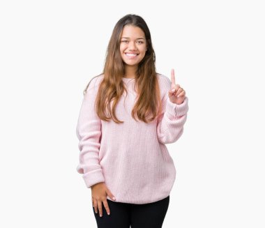 Ve parmak gülümseyen süre bir numara ile kendinden emin ve mutlu yukarıyı gösteren izole arka plan üzerinde pembe kış kazak giyen genç güzel esmer kadın.