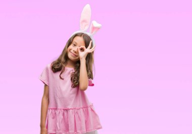 Esmer İspanyol kız mutlu yüz el parmaklarının arasından seyir göz üzerinde ok işaretiyle yapıyor gülümseyen ile Paskalya tavşan kulakları giyiyor