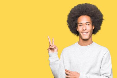 Afrikalı-Amerikalı genç afro saçlı gülen yüz zafer işareti yaparken kameraya göz kırpıyor ile gülümseyen sportif kazak giyiyor. İki numaralı.