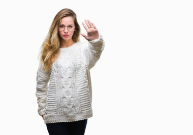 Genç güzel sarışın kadın giyiyor kış kazak ve güneş gözlüğü izole arka stop yapıyor üzerinde elin avuç ile şarkı. Negatif ve ciddi bir jest yüz ifadesiyle uyarı.