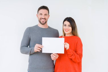 Genç çift boş yaprak kağıt izole arka plan üzerinde duran ve diş gösterilen kendine güvenen bir gülümsemeyle gülümseyerek mutlu bir yüz ile tutarak