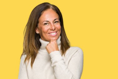 Emin çapraz kollar ve çeneme kaldırdı el ile gülümseme ile kameraya bakarak izole arka plan üzerinde kış kazak giyen güzel orta yaş yetişkin kadın. Pozitif düşünce.