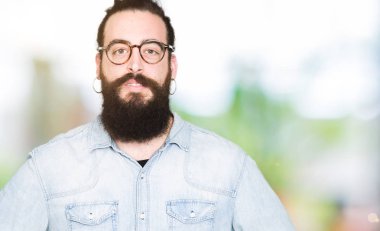 Uzun saç ve sakal gevşek ciddi ifade ile yüzünde gözlüklü genç hipster adam. Basit ve doğal kameraya bakıyor.