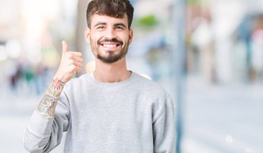 Hareketi el ile mutlu yaşasın yapıyor izole arka plan üzerinde sweatshirt giyen genç yakışıklı adam. Başarı gösteren kameraya bakarak ifade onaylama.