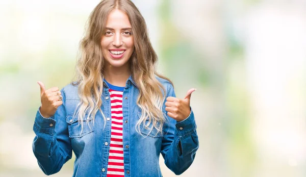 Beautiful young blonde woman over isolated background success sign doing positive gesture with hand, thumbs up smiling and happy. Looking at the camera with cheerful expression, winner gesture.