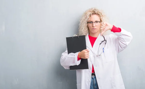 Joven Doctora Rubia Sobre Pared Gris Grunge Sosteniendo Portapapeles Con —  Fotos de Stock