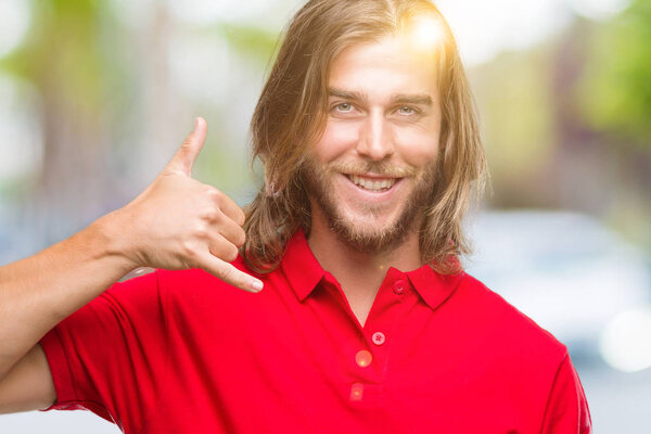 Young handsome man with long hair over isolated background smiling doing phone gesture with hand and fingers like talking on the telephone. Communicating concepts.