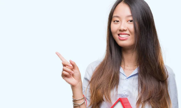 年轻的亚洲妇女真正的国家特工控股的房子孤立的背景非常高兴地指着手和手指的侧面 — 图库照片