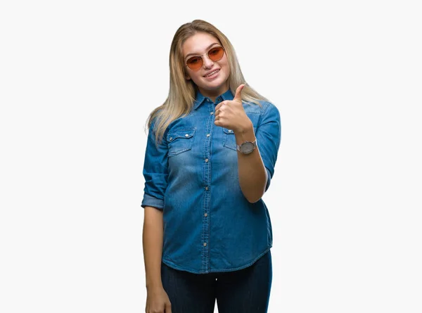 年轻的白种女人戴墨镜在孤立的背景做愉快的拇指手势与手 批准表达式看着相机显示成功 — 图库照片