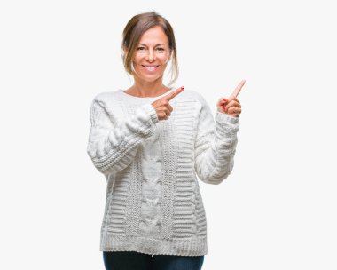 Gülümseyen ve iki elleri ve parmakları ile tarafına işaret kamera bakarak izole arka plan üzerinde kış kazak giyen orta yaş üst düzey İspanyol kadın.