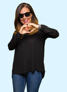 Güzel orta yaş kadın kalp simgesi ve elleriyle şekil gösterilen aşık gülümseyen güneş gözlüğü takıyor. Romantik kavramı.