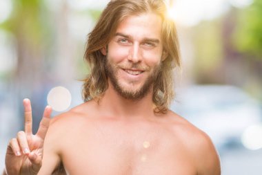 Genç yakışıklı gömleksiz adam uzun saçlı seksi vücut zafer işareti yapıyor parmak gösterilen kamera seyir gülümseyen izole arka plan üzerinde gösterilen. İki numaralı.