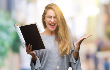 Genç güzel sarışın kadın büyük gülümseme ile çığlık zaferini kutluyor ve ellerini kaldırdı izole arka plan çok mutlu ve heyecanlı, kazanan ifade bir kitap okuma