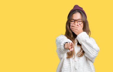 Kış şapka ve gözlük izole üzerinde giyen genç güzel esmer hipster kadın arka plan sizin parmak el kamerasıyla ağzına, utanç ifadesi işaret eden gülme