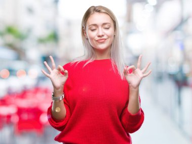 Sarışın genç kadın giyiyor kış kazak izole arka plan üzerinde dinlenmek ve gülümseyen gözlerle kapalı parmak jestle meditasyon yapıyor. Yoga kavramı.