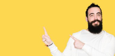 Uzun saç ve sakal gülümseyen ve iki elleri ve parmakları ile tarafına işaret kamera bakarak sportif sweatshirt giyen genç adamla.