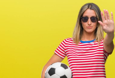 Açık eliyle dur işareti ile ciddi ve kendine güvenen ifade, savunma jest yapıyor izole arka plan üzerinde futbol futbol topu tutan genç güzel kadın