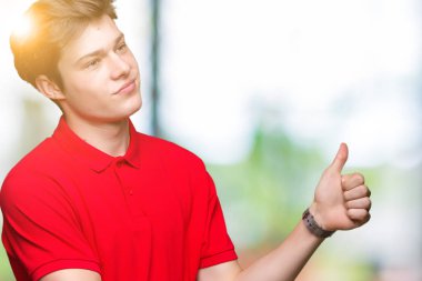 Kırmızı giyen genç yakışıklı adam yanına bir jest yapıyorsun gülümseyen t-shirt gurur, seyir izole arka plan üzerine yaşasın