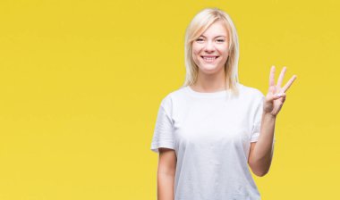 Gösterilen ve parmakları ile işaret izole arka plan üzerinde beyaz t-shirt giyen genç güzel sarışın kadın kendinden emin ve mutlu gülümseyerek iken üçüncü.