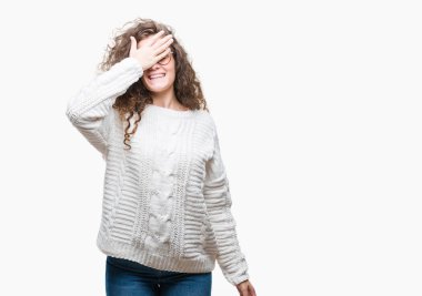 Güzel esmer kıvırcık saçlı Genç kız gülümsüyor ve gözleri için sürpriz kapsayan yüz el ile gülüyor izole arka plan üzerinde kış kazak giyiyor. Kör kavramı.