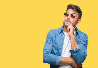 Genç yakışıklı adam çene düşünme hakkında soru, dalgın ifade üzerine el ile izole arka plan üzerinde güneş gözlüğü takıyor. Düşünceli yüzüyle gülümsüyor. Şüphe kavramı.