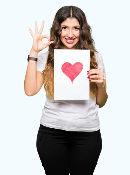 Młoda Kobieta Dorosłych Posiadających Kartę Czerwonym Sercem Robi Znak Palcami — Zdjęcie stockowe