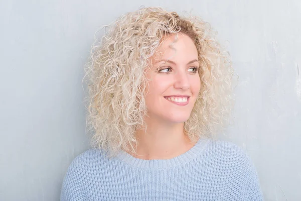 年轻的金发女人与卷曲的头发在垃圾灰色背景看着一边与微笑的脸上 自然的表达 笑的自信 — 图库照片