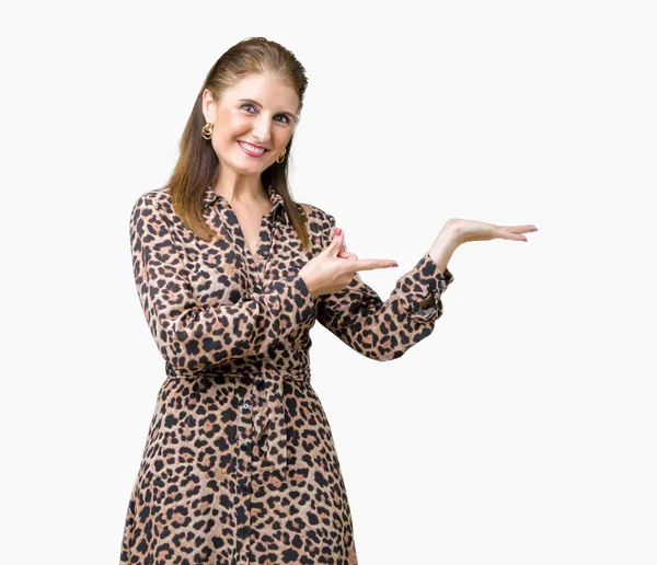 Hayret ve el ile sunulması ve parmak ile işaret ederken kameraya gülümseyen izole arka plan üzerinde leopar elbise giyen güzel orta yaş olgun zengin kadın.
