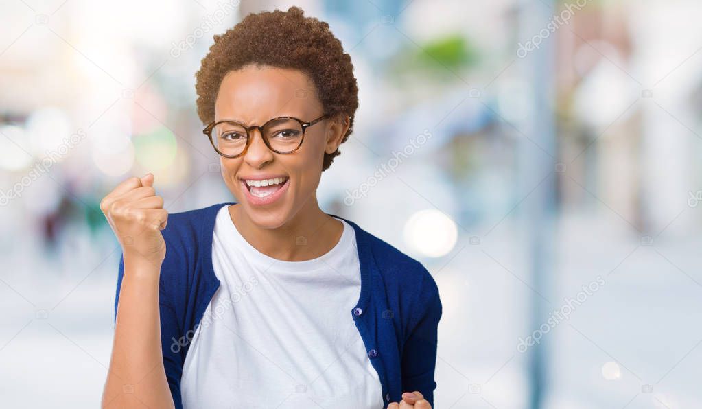 Young beautiful african american woman wearing glasses over isolated background very happy and excited doing winner gesture with arms raised, smiling and screaming for success. Celebration concept.