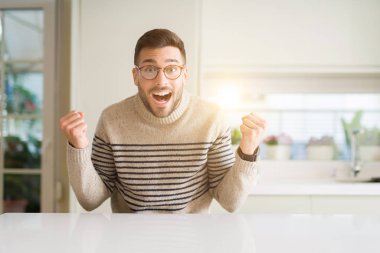 Evde gözlüklü genç yakışıklı adam şaşırmış ve başarı için hayran kaldırdı kollarını açarak kutluyor ve gözleri açık. Kazanan kavramı.