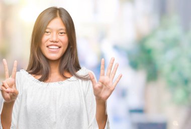 Genç Asyalı kadın gösterilen ve parmakları ile işaret izole arka plan üzerinde kendinden emin ve mutlu gülümseyerek süre yedi numara.