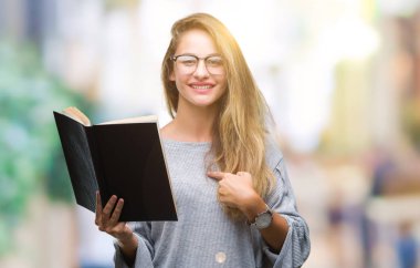 Genç güzel sarışın kadın kendisine sürpriz yüz işaret parmağı izole arka plan üzerine bir kitap okuma