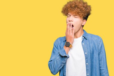 Afro saçlı kot ceket giyen genç yakışıklı adam el ağzıyla kapsayan yorgun esneme sıkılmış. Restless ve uyku hali.