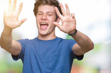 Üzerinde gösterilen ve parmakları ile işaret izole arka plan mavi t-shirt giyen genç yakışıklı adam numara 9 kendinden emin ve mutlu gülümseyerek süre.