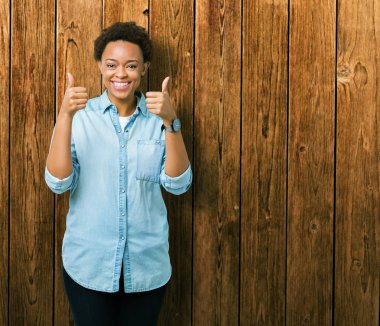 Genç güzel Afrikalı-Amerikalı kadın el ile pozitif jest yapıyor izole arka plan başarı işareti yüzünden başparmak gülümseyen ve mutlu. Neşeli bir ifadeyle, kazanan jest kameraya bakıyor.