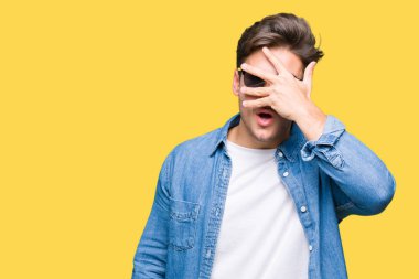 Mahcup ifadeyle parmaklarımın arasından seyir yüz ve gözler el ile kapsayan şok bakmak izole arka plan üzerinde güneş gözlüğü takmış genç yakışıklı adam.