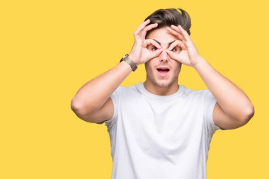 Dilini, parmaklarının arasından baktığını yapışmasını dürbün gibi ok jest yapıyor izole arka plan üzerinde beyaz t-shirt giyen genç yakışıklı adam. Deli ifade.