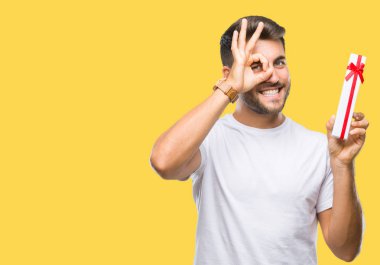 Mutlu yüz el parmaklarının arasından seyir göz üzerinde ok işaretiyle yapıyor gülümseyen izole arka plan üzerinde Sevgililer günü hediyesi veren aşık genç yakışıklı adam