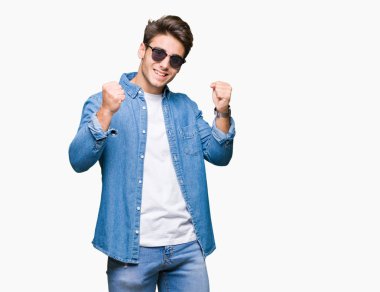 Yakışıklı delikanlı izole arka plan kutlama üzerinde güneş gözlüğü takıyor şaşırttı ve başarı için kaldırdı kollarını açarak hayret ve gözleri açık. Kazanan kavramı.