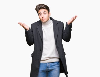 Üzerinde kış ceket giyen genç zarif adam arka plan clueless ve şaşkın bir ifadeyle kollar ve eller kaldırdı izole. Şüphe kavramı.